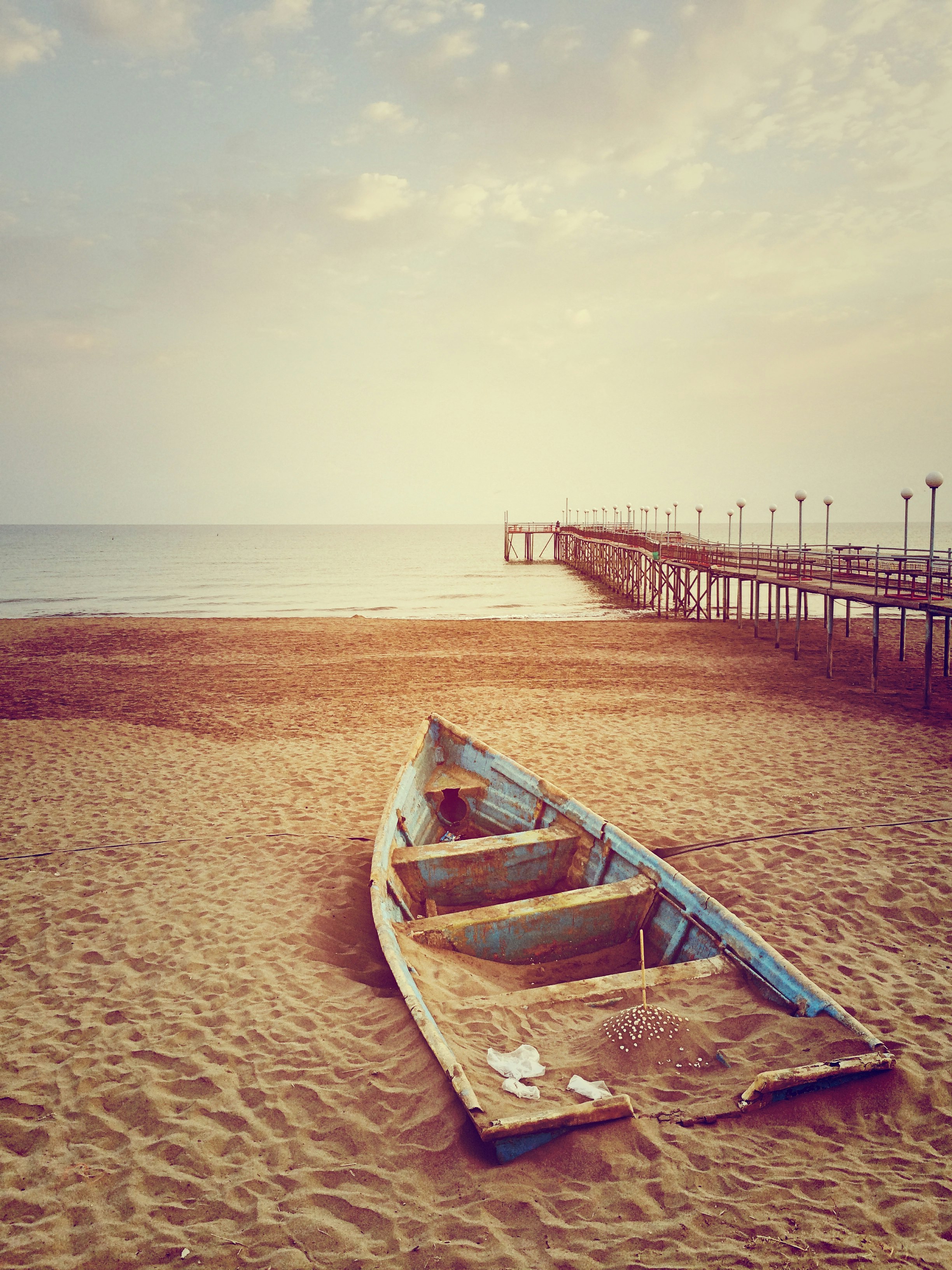 blue canoe boat on brown sand near brown wooden dock and body of water during daytime